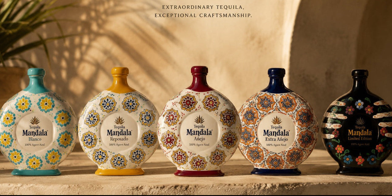 Five decorative tequila bottles from Mandala Tequila are lined up on a stone surface against a warm sunlit wall with leaf shadows. The bottles feature intricate hand-painted patterns in various colors including yellow, blue, red, and black, with white labels in the center.
