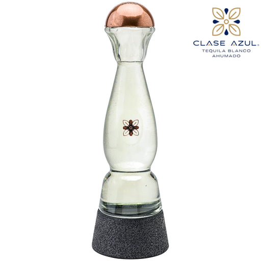 A clear glass tequila decanter with a copper-colored top, a small black floral emblem on the front, and a textured dark gray base. The Clase Azul logo is visible in the upper right corner against a plain white background.