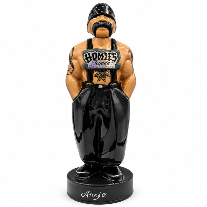 A glossy ceramic figurine of a biker-style man with a black mustache and black overalls, standing on a black base labeled 'Anejo'. The figurine has a tan skin tone and a 'Homies Tequila' patch on the chest.